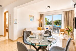 A hotel room with a dining area, a bed, a TV, and a view of the pool.