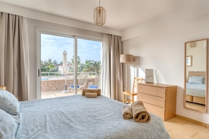 A bedroom with a large bed, a wooden dresser, a mirror, and a view of a pool and outdoor seating.