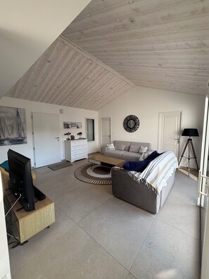 A modern living room with a high ceiling, a sofa, a coffee table, a TV, and a painting on the wall. - House, villa with a year-round heated indoor pool set at 31° (St jean de monts)