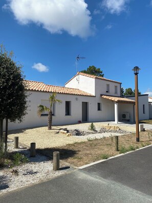 A two-story building with a tiled roof, a small garden with gravel and plants, and a clear blue sky. - House, villa with a year-round heated indoor pool set at 31° (St jean de monts)
