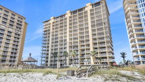 A beachfront hotel with multiple floors, balconies, and a sandy beach area with a small structure.