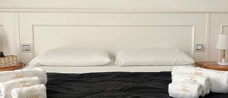 A hotel room with a bed, white pillows, a black bedspread, and a framed coastal landscape painting above the bed.