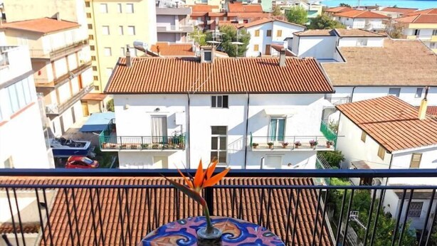 A balcony with a tiled floor, two chairs, and a table with a decorative centerpiece. - Hotel Tea Praia  (Praia a Mare)
