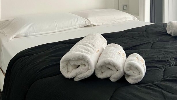 A hotel room with a bed, white headboard, and a painting of a coastal landscape. - Hotel Tea Praia  (Praia a Mare)