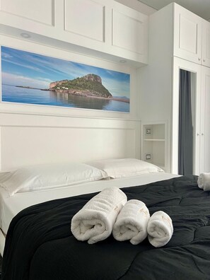 Habitación de hotel con cama, cabecera blanca y un cuadro de un paisaje costero.