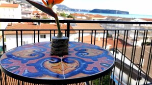 A round table with a decorative pattern, a potted plant, and a view of a coastal town. - Hotel Tea Praia  (Praia a Mare)