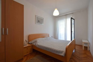 A bedroom with a wooden bed, a nightstand, a desk, a wardrobe, a hanging light, a framed picture, and a window with curtains.
