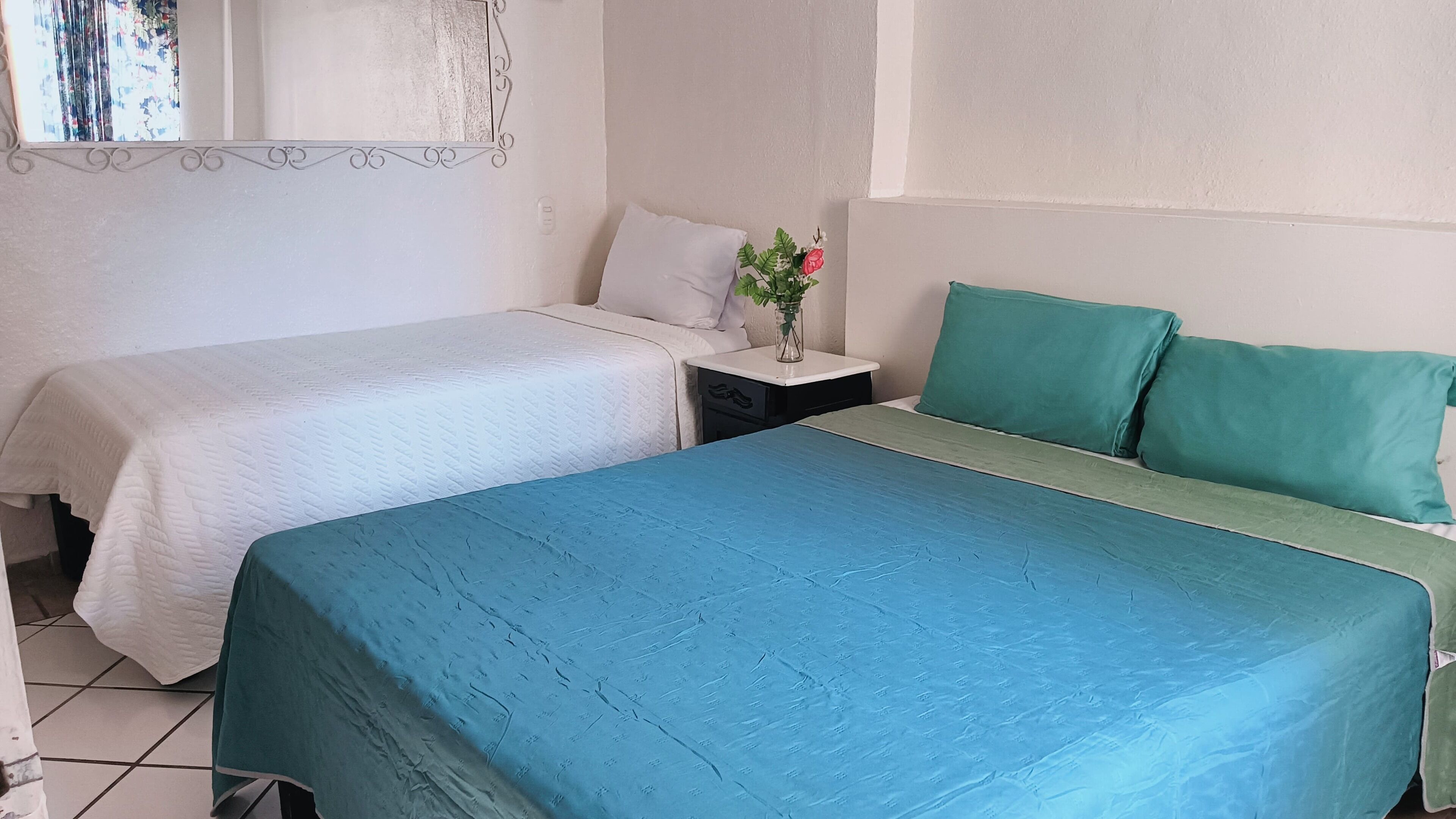 A room with two beds, a nightstand with a vase of flowers, and a white wall with a decorative border.