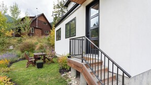 Une maison moderne dotée d’une terrasse en bois, d’un escalier et d’un jardin agrémenté de diverses plantes et d’une table.