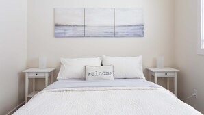 Une chambre à coucher bien aménagée, avec un lit, deux tables de chevet, une œuvre d’art accrochée au mur et un coussin décoratif.