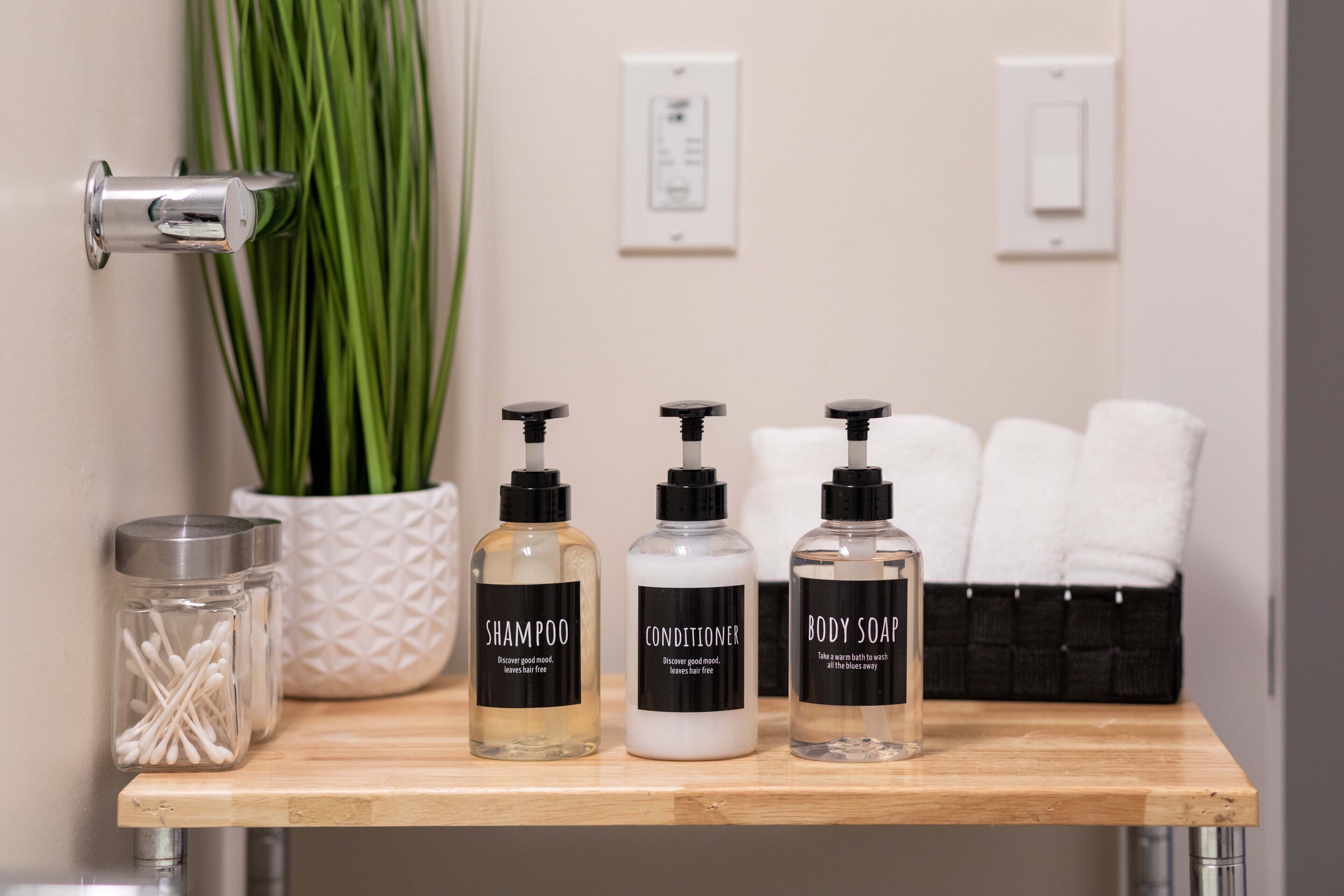 Une étagère de salle de bain avec trois bouteilles de shampoing, d’après-shampoing et de savon liquide, une plante en pot et un panier rempli de serviettes.
