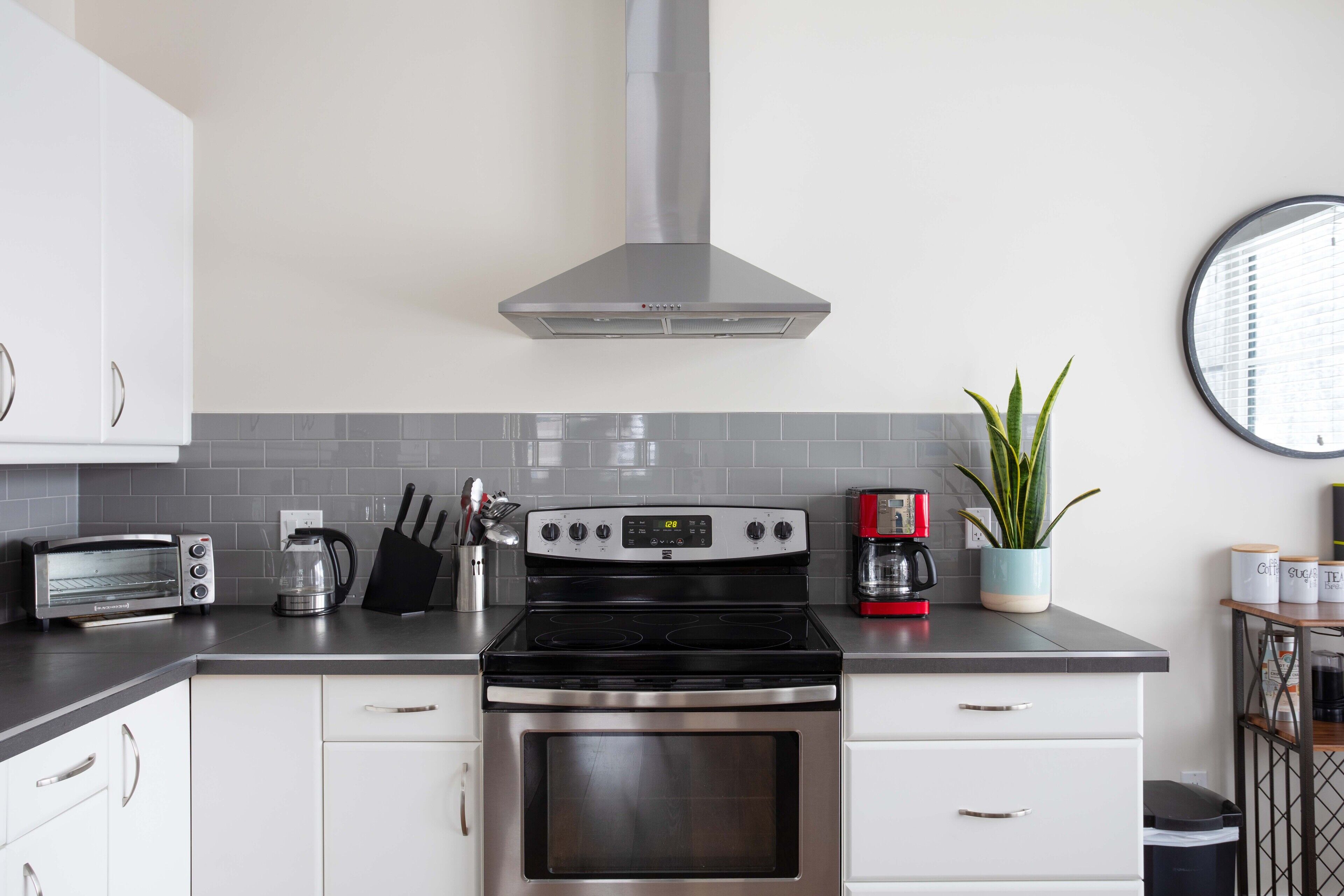 Una cocina moderna con campana de acero inoxidable, horno empotrado, cafetera y tostadora.
