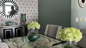 A dining area with a glass table, two vases with flowers, patterned wallpaper, a mirror, and a wall-mounted sign. - Biloxi border, huge King size Condo (Gulfport)