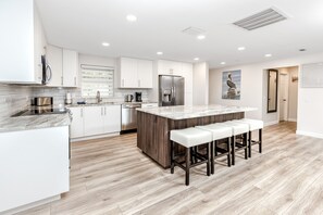 A modern kitchen with white cabinets, a marble island, stainless steel appliances, and a wooden floor. - Pelican House · Game Room, Pool, 5 min to Beach (Tarpon Springs)