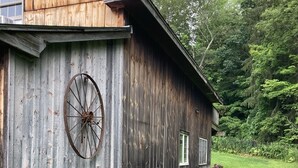 Un graner de fusta rústic amb una roda gran subjecta al costat, envoltat d'un pràt meticulosament cuidat i arbres densos al fons.