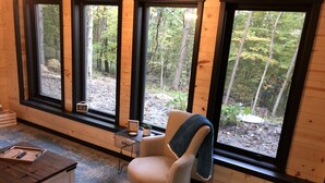 Une pièce confortable avec de grandes fenêtres, un fauteuil, une petite table et un meuble en bois.