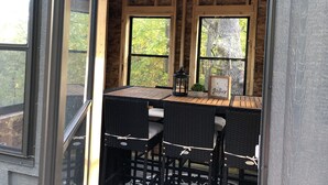 Un espace extérieur accueillant, avec une table et des chaises, de grandes fenêtres et un ventilateur.