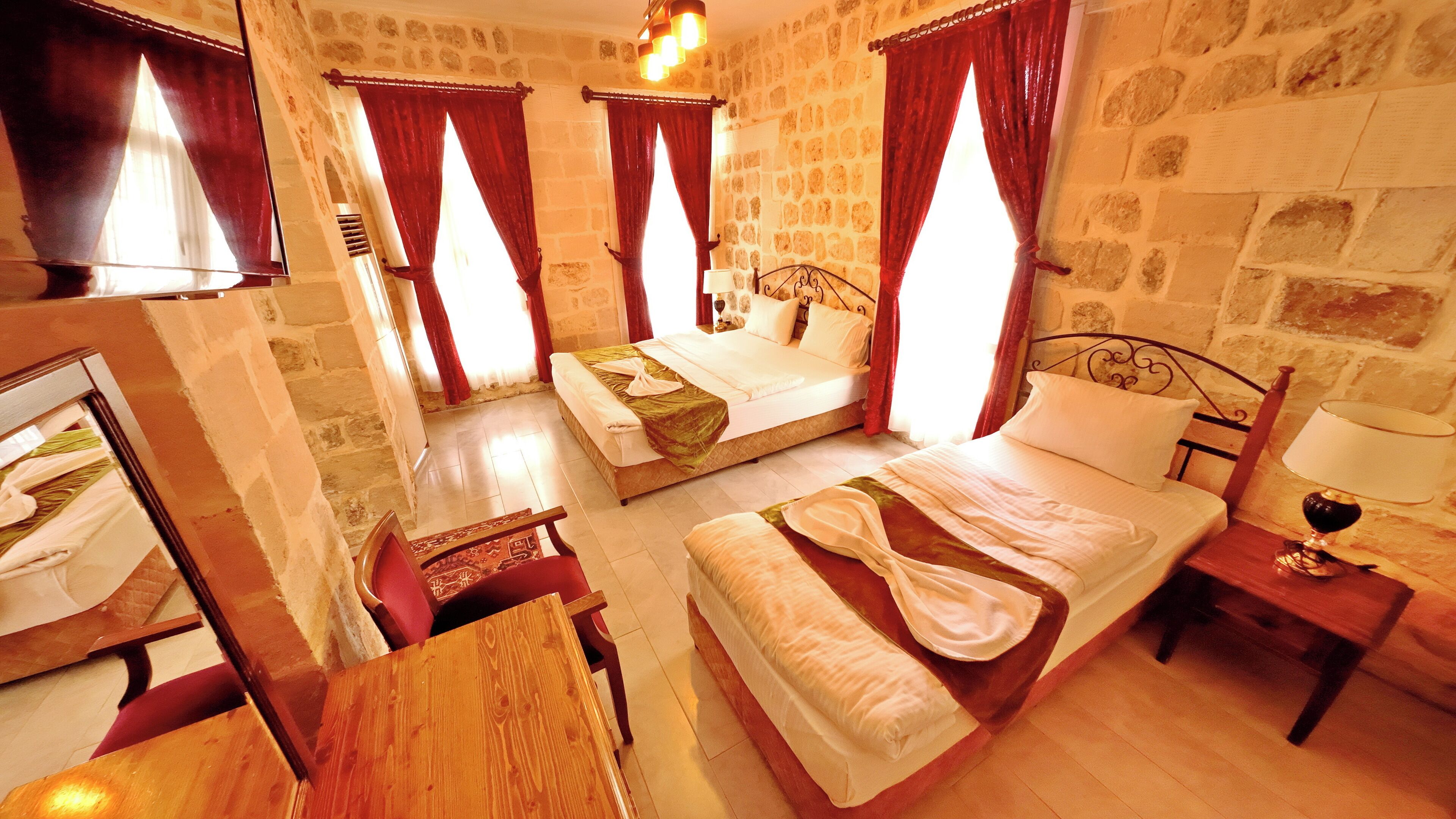 Una habitación de hotel con pared de piedra, una cama con cabecero de madera, una mesita de noche con lámpara y una silla.