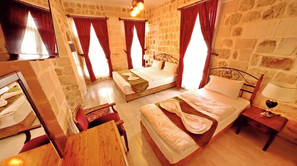 Una habitación de hotel con pared de piedra, una cama con cabecero de madera, una mesita de noche con lámpara y una silla.