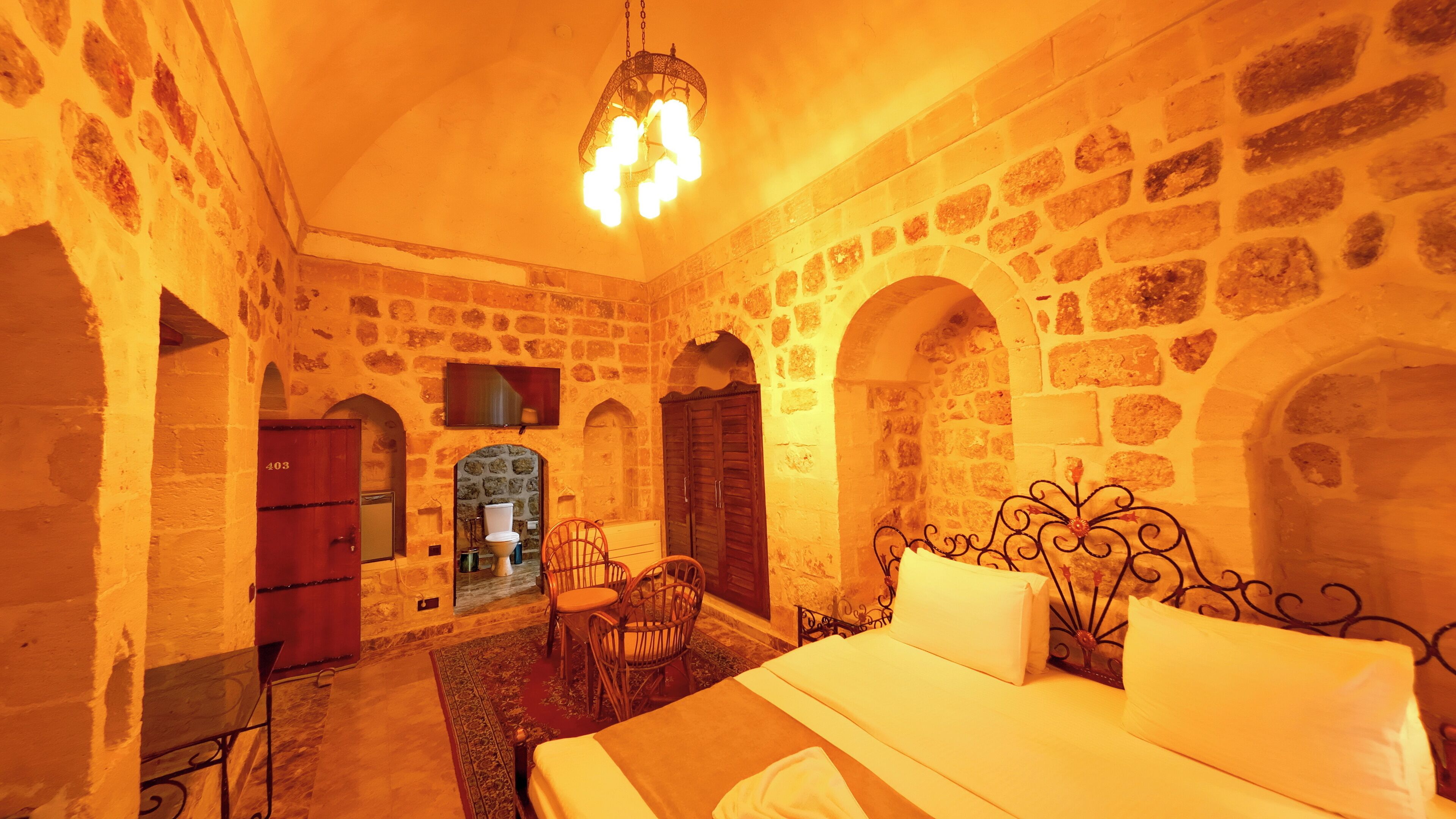 A room with stone walls, a bed, a chair, a TV, and a fireplace.