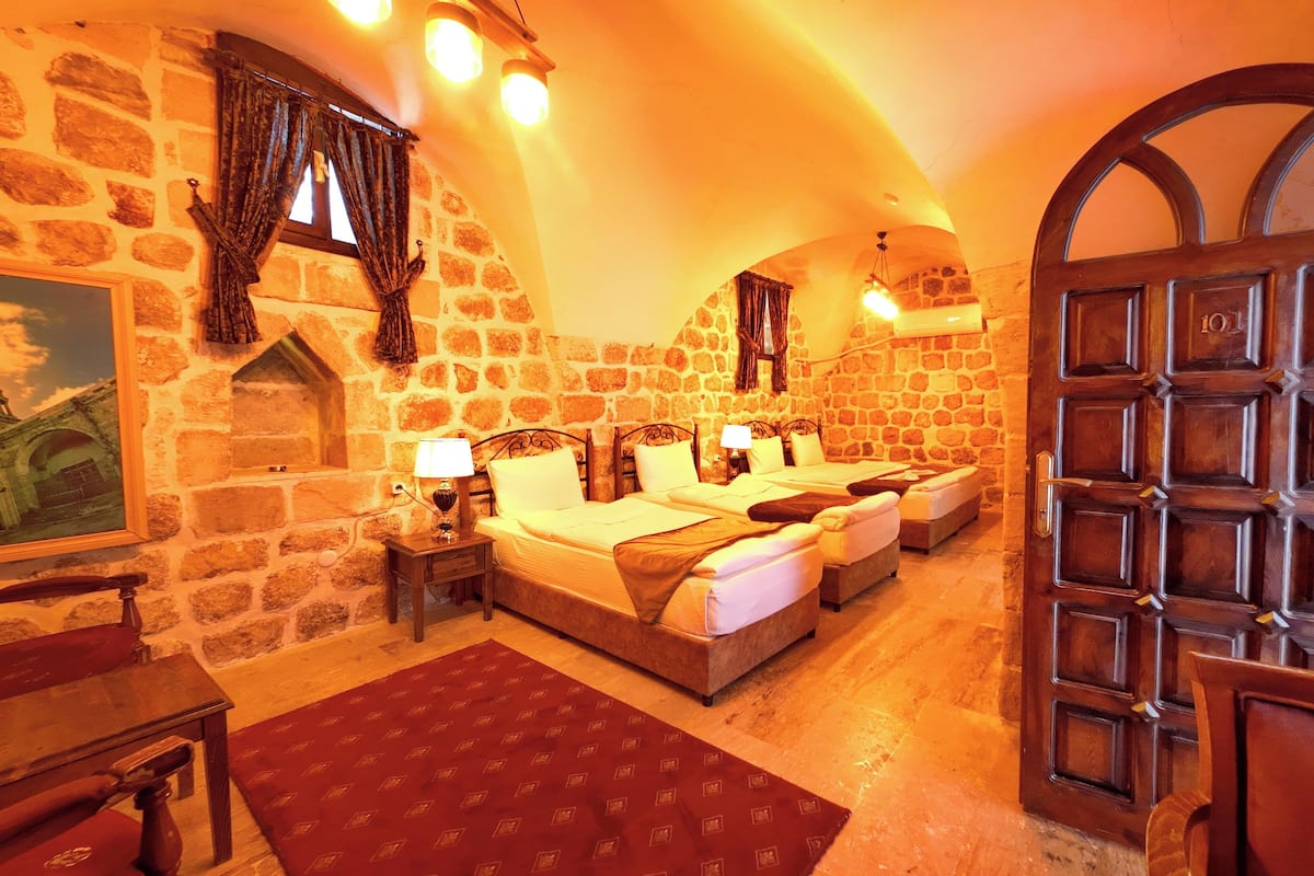 Una habitación con paredes de piedra, una puerta de madera y una cama con dos almohadas.