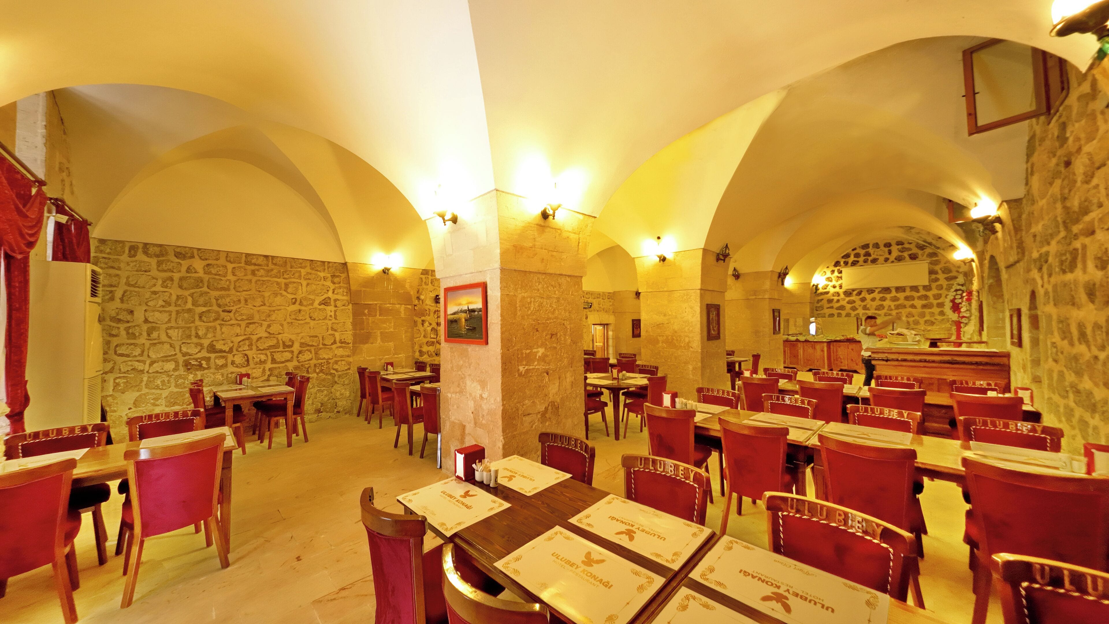 A restaurant with stone walls, arched ceilings, and red chairs. Tables are set with menus and place settings.