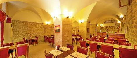 A restaurant with stone walls, arched ceilings, and red chairs. Tables are set with menus and place settings.