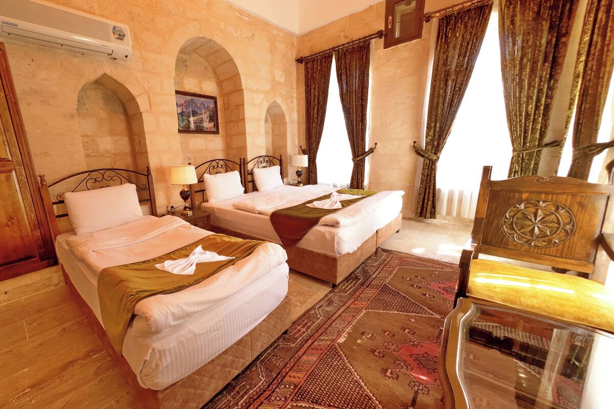 Habitación de hotel con dos camas, armario de madera, paredes de piedra en arco y una alfombra tradicional.