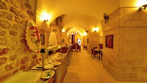 A long corridor with stone walls and arched ceilings, leading to a dining area with tables and chairs. - Ulubey Konagi (Mardin)