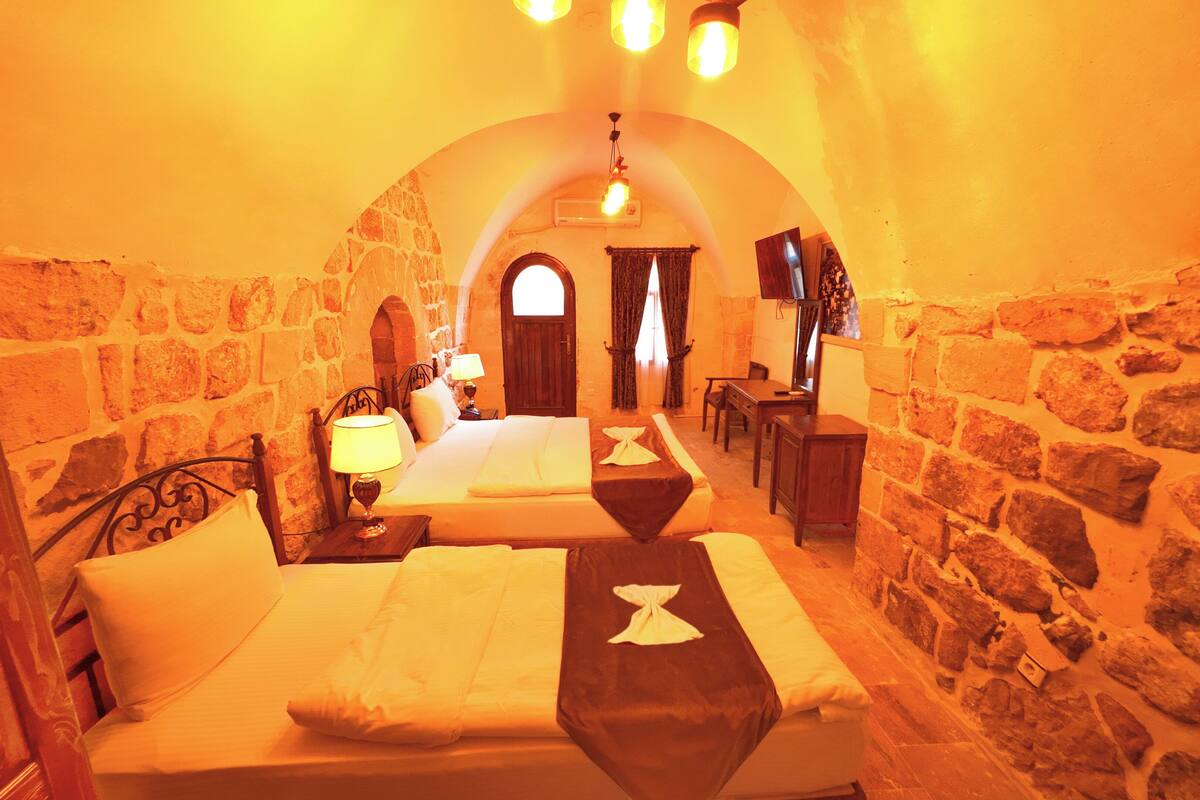 Una habitación acogedora con paredes de piedra, dos camas, un escritorio y un televisor.