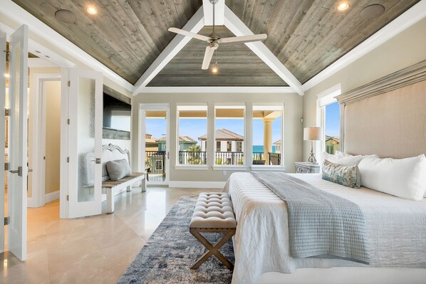 A spacious bedroom with a large bed, a ceiling fan, and a view of the ocean through large windows.