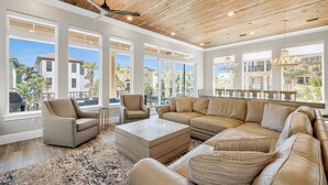 A spacious living room with a large sectional sofa, a coffee table, and a chair. The room has large windows offering views of the outside. - 7BR Gulf Views, Large Private Pool/Spa, Private Beach/Gated Community, Sleeps 20 (Destin)