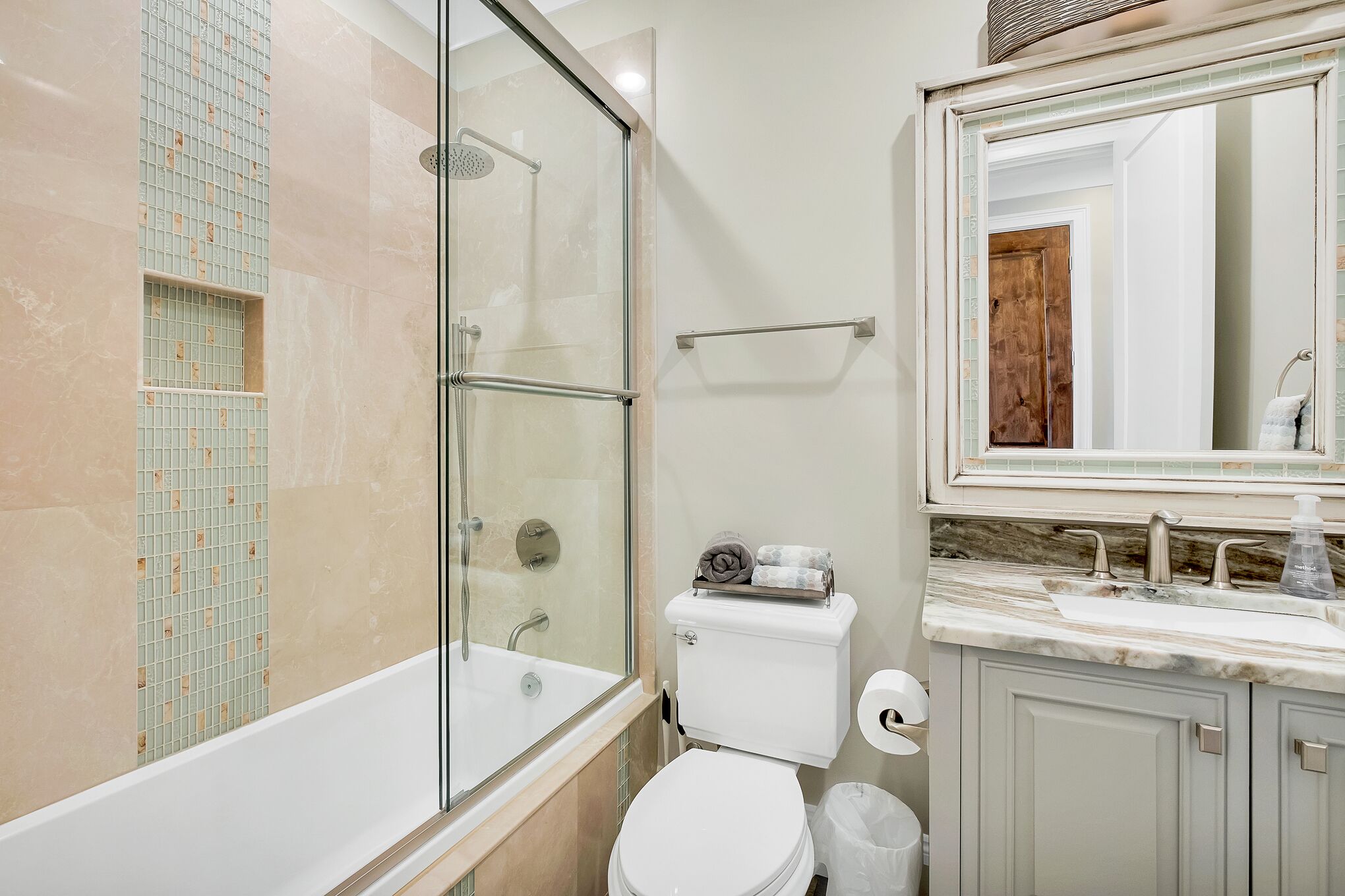 A modern bathroom with a glass-enclosed shower, a white toilet, and a marble countertop with a sink and mirror.