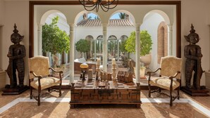 A spacious lobby with a central seating area, two wooden statues, and a view of an outdoor courtyard through an arched window. - Cubo's Mountain Bayview Luxury Villa / views / free wifi / gym (Málaga)