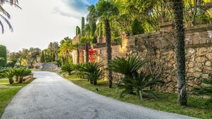 A paved pathway flanked by palm trees and a stone wall, leading to a building with a traditional architectural style. - Cubo's Mountain Bayview Luxury Villa / views / free wifi / gym (Málaga)