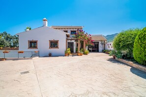 A traditional white building with a tiled roof, a courtyard with potted plants, and a view of a mountain range.