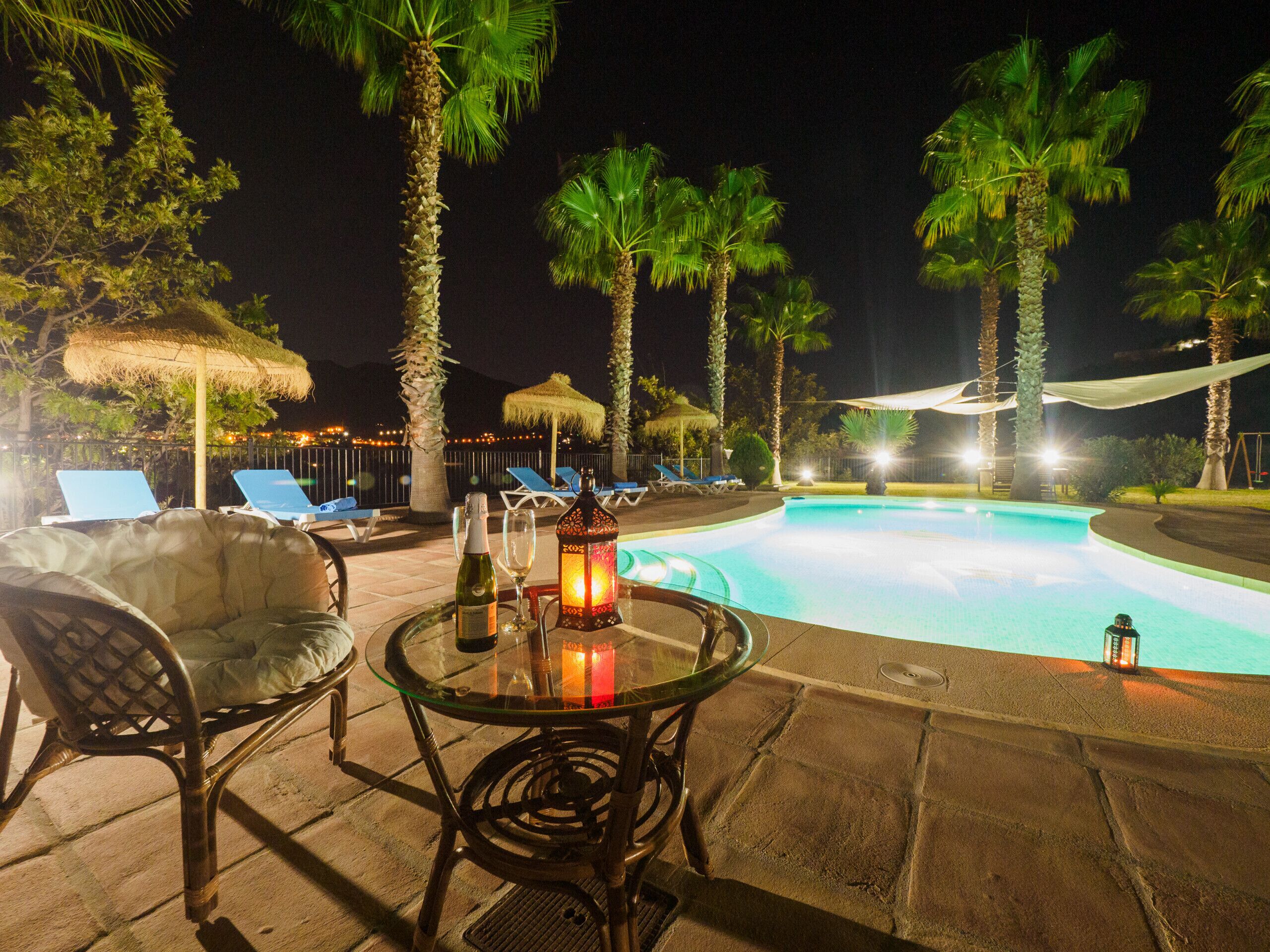 A poolside area with lounge chairs, a table with a bottle and glasses, and a lantern.