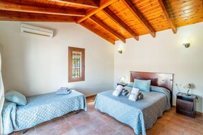 A bedroom with two beds, a window with a view, a wooden ceiling, and a wall-mounted air conditioner.