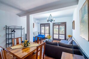 A dining area with a wooden table and chairs, a sofa, and a chandelier.