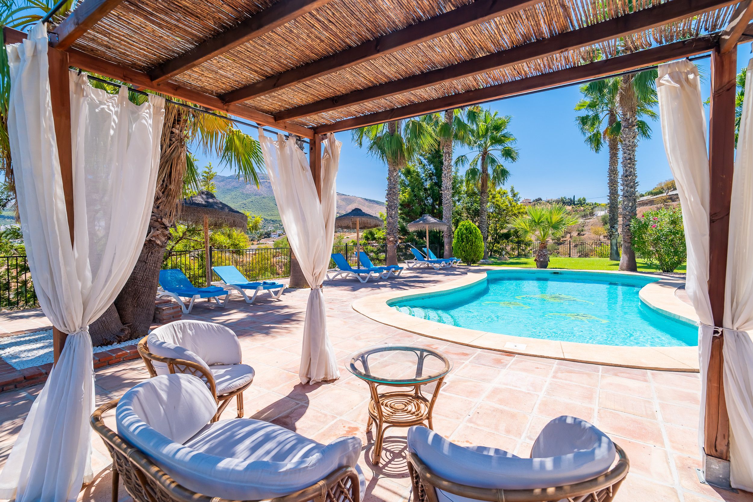 A covered outdoor area with a pool, lounge chairs, and a view of the landscape.