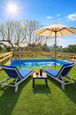 Ein Poolbereich mit zwei Liegestühlen, einem Tisch mit Flasche und Glas sowie einem großen Sonnenschirm.