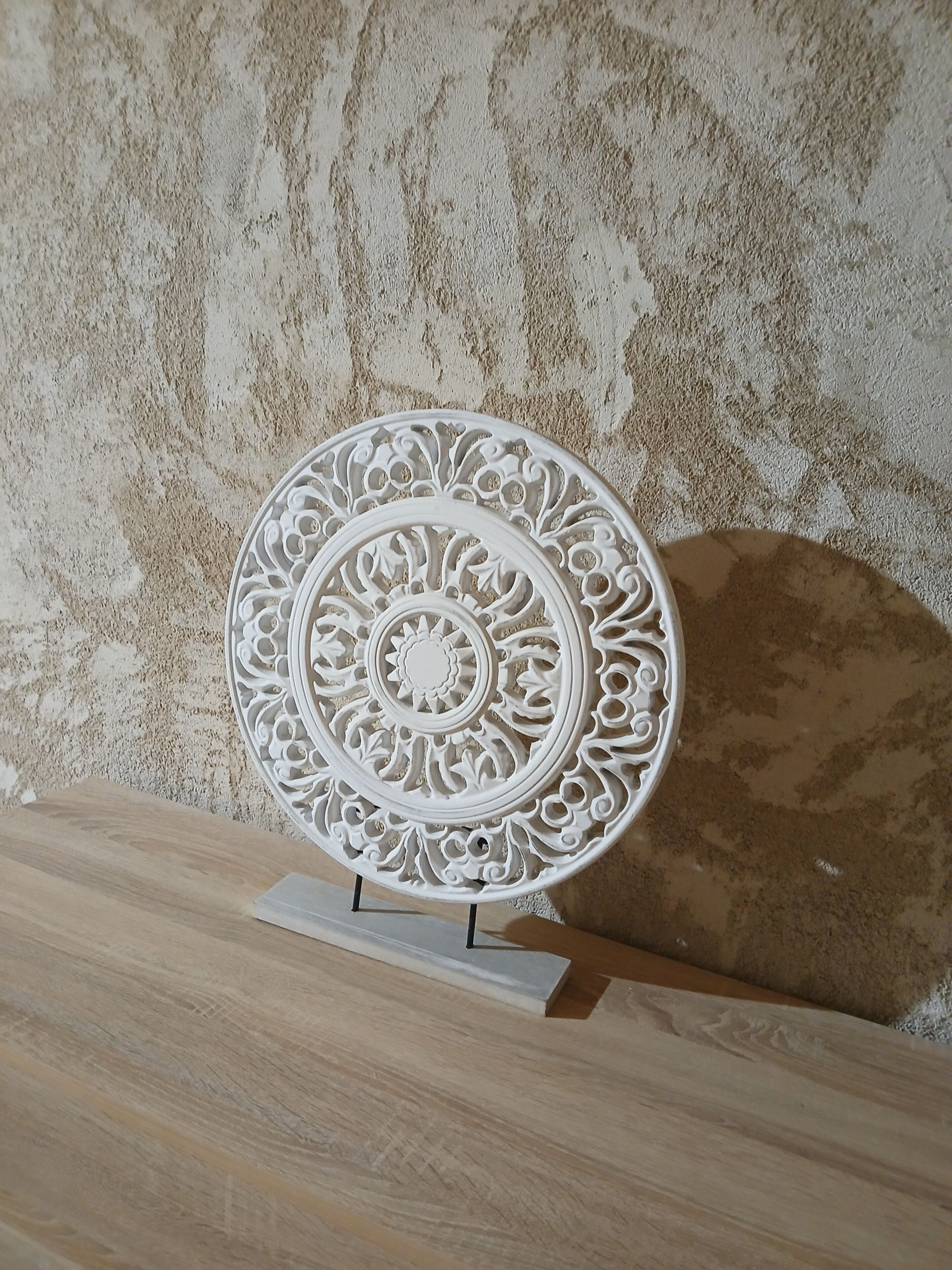 A decorative plate with intricate patterns on a stand against a textured wall.