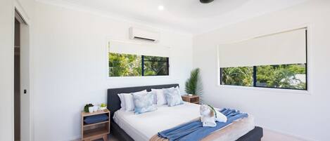 A modern bedroom with a bed, bedside tables, a ceiling fan, and a large window with a view of greenery.