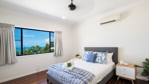Quarto com uma janela grande, cama com roupa de cama estampada, mesa de cabeceira e ventilador de teto.