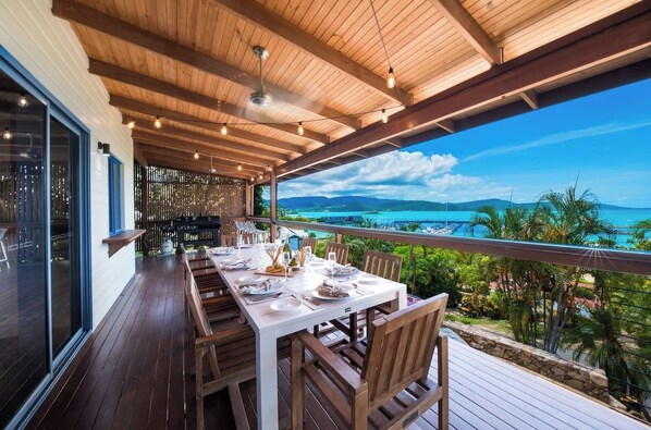 An outdoor dining area with a wooden deck, a table set for two, and a view of the ocean and mountains.
