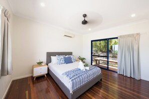Une chambre à coucher avec un lit, une table de chevet et une vue sur un jardin, visible à travers une porte vitrée.
