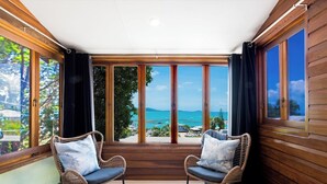 Quarto com duas cadeiras de vime, uma janela grande com vista para o mar e paredes de madeira.