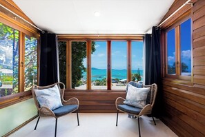 A room with two wicker chairs, a large window with a view of the sea, and wooden walls. - Beyond The Palms (Airlie Beach)