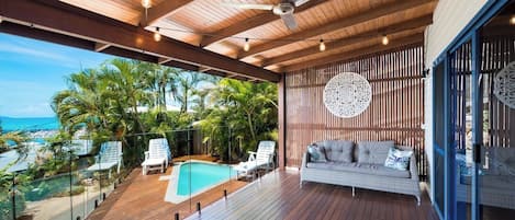 A wooden deck with a pool, lounge chairs, and a sofa with a view of the ocean.