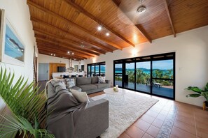 A spacious living area with a large gray sofa, a white coffee table, and a view of the outdoors through large sliding glass doors. - Beyond The Palms (Airlie Beach)